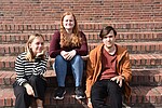 Drei junge Menschen sitzen auf einer Außentreppe und blicken in die Kamera.