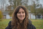 Sophia hat lange Haare und blickt freundlich in die Kamera, im Hintergrund wiese und ein Gebäude.