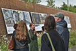 Führung zur Installation "Wie lange werden wir hier sein?" mit Personen vor großformatigen Fotos in der Fuge draußen am denk.mal