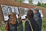 Führung zur Installation "Wie lange werden wir hier sein?" mit Personen vor großformatigen Fotos in der Fuge draußen am denk.mal