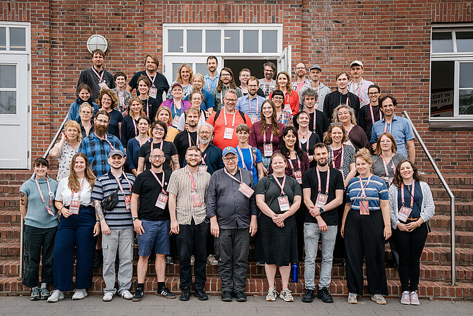 RememBarcamp 2026 Gruppenfoto mit ca. 60 Personen, die auf Stufen stehen vor dem Studienzentrum in der KZ-Gedenkstätte Neuengamme