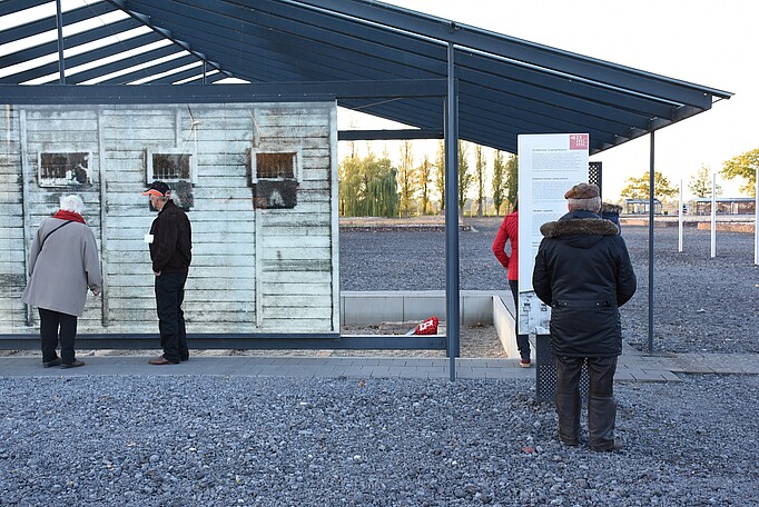Foto von vier Besucherinnen und Besuchern, die vor einer Installation am ehemaligen Arrestbunker stehen und sich Bilder und Texte ansehen