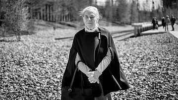 Eine weißhaarige Frau mit einem dunklen Cape und rotem Pullover steht am denk.mal Hannoverscher Bahnhof vor einem Steinfeld