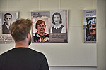 Die Ausstellung mit drei Panels ist zu sehen. Auf jedem Panel sind zwei Fotos. Eine Person steht davor und sieht sie sich an.
