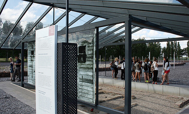 Foto einer Führung für eine Gruppe an den Grundmauern des ehemaligen Arrestbunkers. Foto: KZ-Gedenkstätte Neuengamme, 2014.