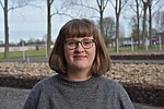 Clara Mansfeld trägt eine Brille und ein graues Kleid, sie blickt lächelnd in die Kamera, im Hintergrundbäume.