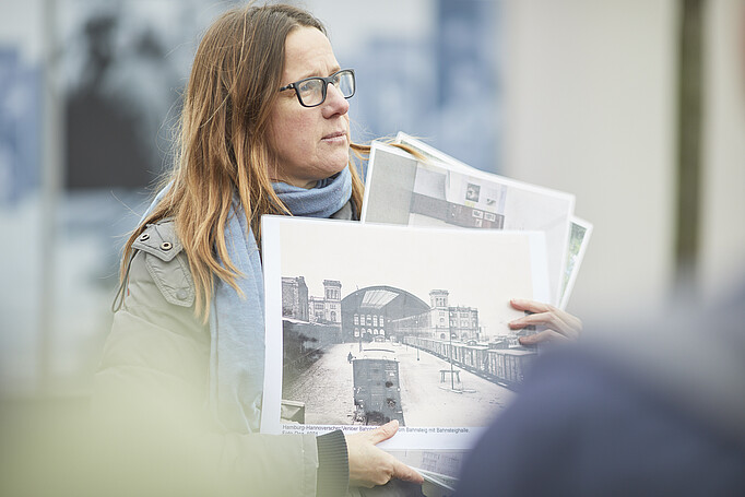 Karin Heddinga hält Ausdrucke historischer Fotos des Hannoverschen Bahnhofs hoch.