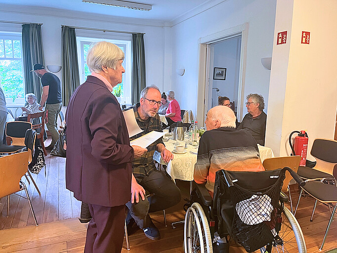 Ein Mann im Rollstuhl sitzt an einem Tisch mit einem Mann, der sich mit ihm unterhält. 