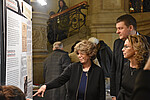 Drei Personen vor einer Ausstellungstafel, eine Person deutet auf ein Detail auf der Tafel