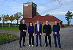 Fünf Personen in dunkelblauer Kleidung stehen am ehemaligen Wachturm in der KZ-Gedenkstätte Neuengamme