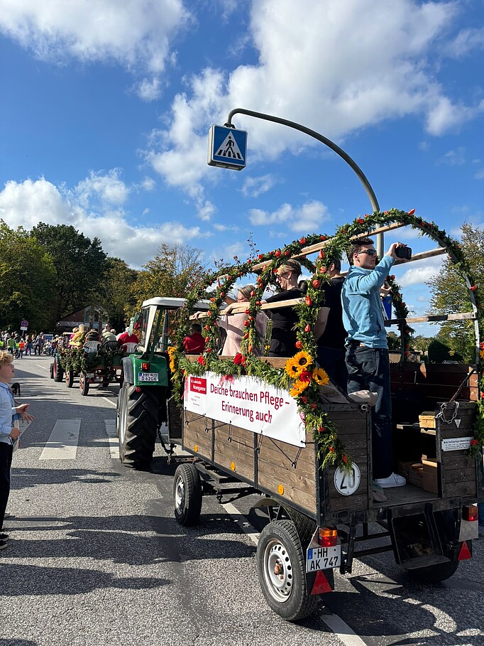 Erntedankumzug durch Kirchwerder mit Wagen der Gedenkstätte, die hinter einem anderen Wagen auf der Straße herfährt, am Rande Zuschauer