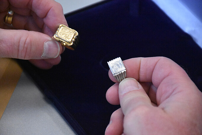 Ein goldener und ein silberner Herrenring werden von zwei Händen gehalten