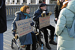 Zwei ältere Menschen sitzen auf Rollatoren und halten Plakate in der Hand. Um sie herum mehrere andere Personen. Im Hintergrund die Arkaden an der Alster.