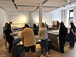 Viele Personen stehen in einem Ausstellungsraum und lesen Ausstellungstexte.