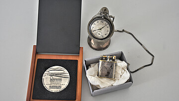 drei Objekte aus dem Nachlass Zegers: Ein Feuerzeug, eine Taschenuhr, eine Medaille