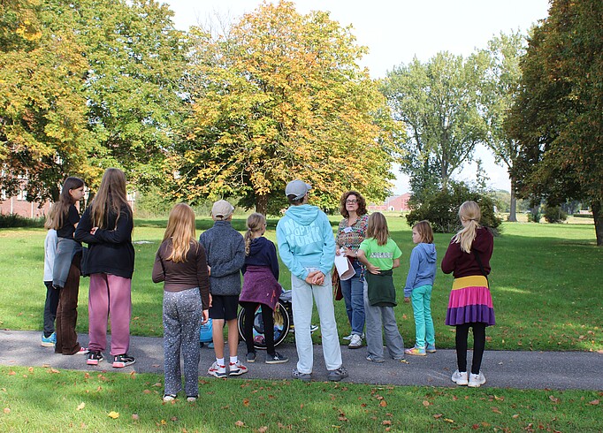 Kinder stehen um einen Guide herum, im Hintergund das Klinkerwerk und Bäume.