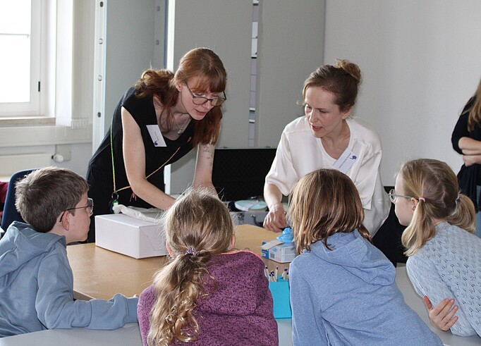 Kinder und Archivarin versammeln sich um eine Archivbox.