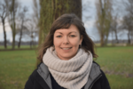 Malina trägt einen großen Wollschal und eine Jacke. Im Hintergrund Wiese und Bäume
